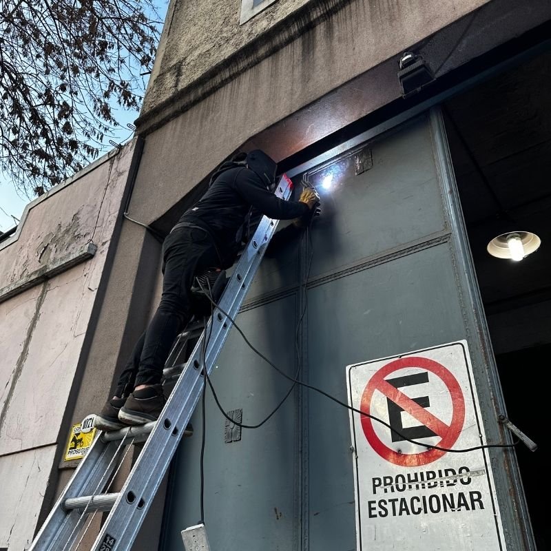 Reparación de portón pivotante de gran altura. Reparación general en un portón pivotante o batiente de doble hoja, con una altura de 6 metros y un ancho aproximado de 1.60 metros por hoja. Se realizó el cambio del pivote inferior con mecanizado y bolilla de acero, además de ajustes en el marco superior. Trabajo realizado por HERREELEC.